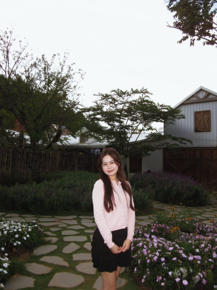 Anna in a pink cardigan standing in a flower garden